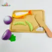 My Little Cooking Playset wooden cutting board with colorful toy fish, green vegetable pieces and a wooden knife, alongside a purple toy vegetable separated into pieces for pretend cooking.